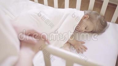 一个穿着白色衣服的女人站在<strong>婴儿床</strong>旁边，<strong>婴儿床</strong>上睡着一个小孩